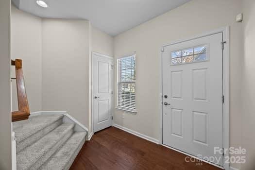 entrance foyer with dark wood-style flooring, stairway, and baseboards