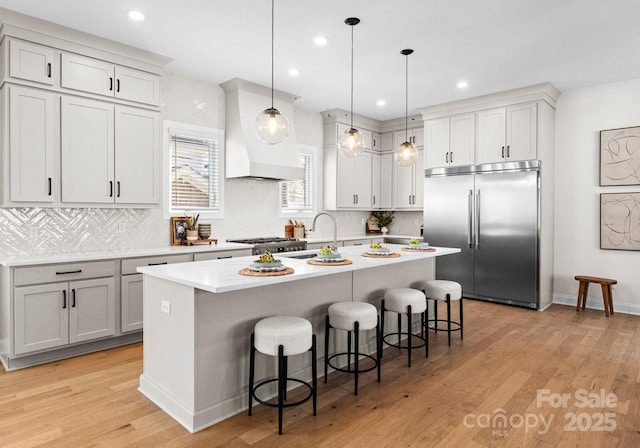 kitchen featuring custom range hood, a kitchen breakfast bar, built in refrigerator, hanging light fixtures, and light countertops