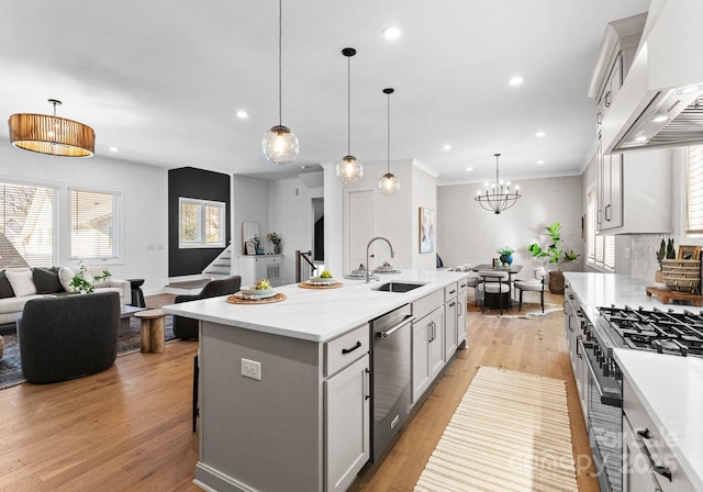 kitchen with stainless steel appliances, a sink, hanging light fixtures, custom exhaust hood, and a center island with sink