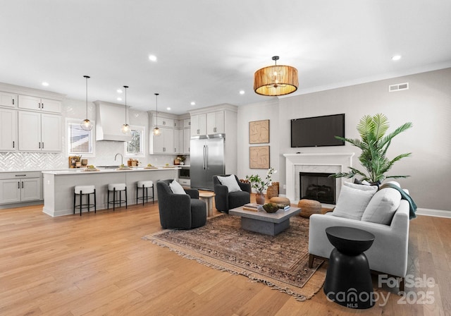 living room featuring a fireplace, recessed lighting, visible vents, light wood-style flooring, and ornamental molding