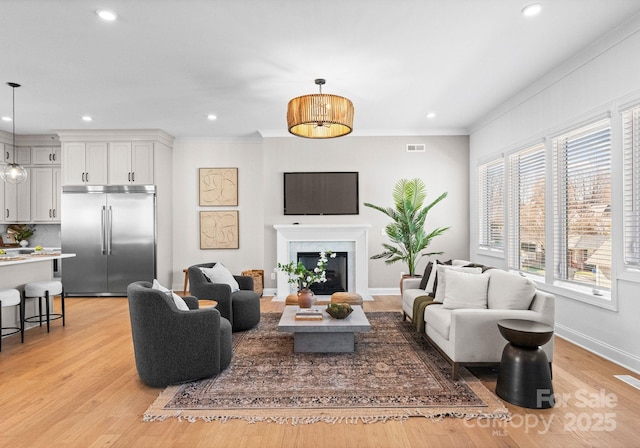 living area featuring light wood-style flooring, visible vents, crown molding, and a glass covered fireplace