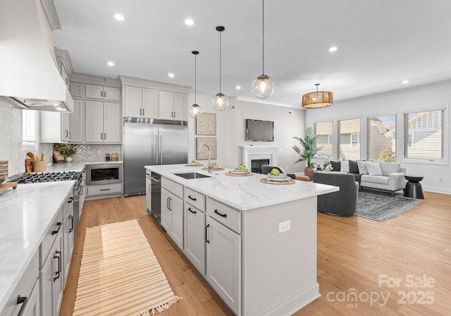 kitchen featuring a kitchen island with sink, a sink, open floor plan, custom range hood, and pendant lighting