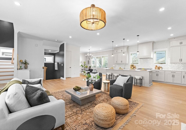 living room featuring baseboards, stairway, an inviting chandelier, light wood-style floors, and recessed lighting