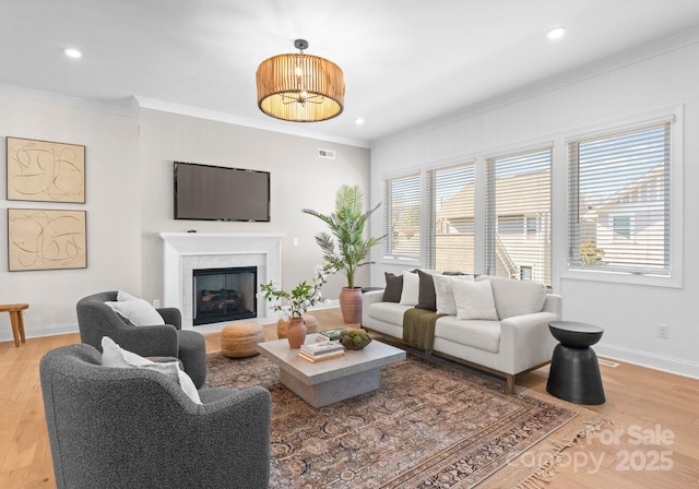 living room with ornamental molding, baseboards, a fireplace, and light wood finished floors