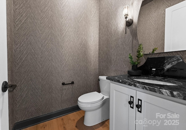 bathroom with toilet, wood finished floors, vanity, and wallpapered walls