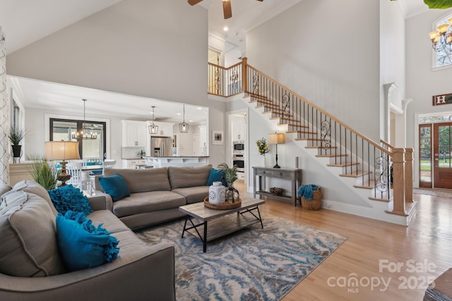 living area with ceiling fan with notable chandelier, stairway, wood finished floors, and crown molding