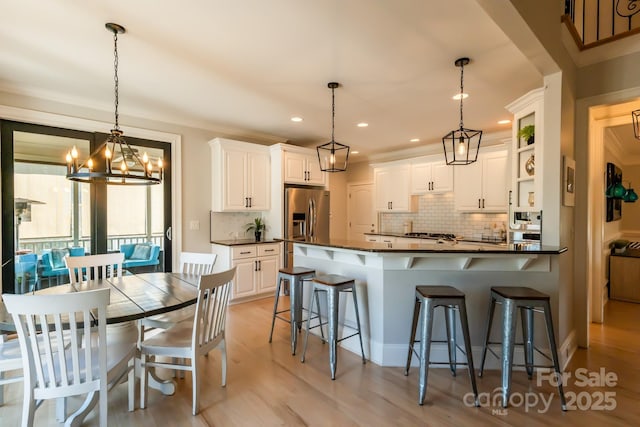 kitchen featuring stainless steel refrigerator with ice dispenser, dark countertops, white cabinetry, and a kitchen breakfast bar