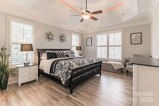 bedroom featuring ornamental molding, light wood-type flooring, a raised ceiling, and ceiling fan