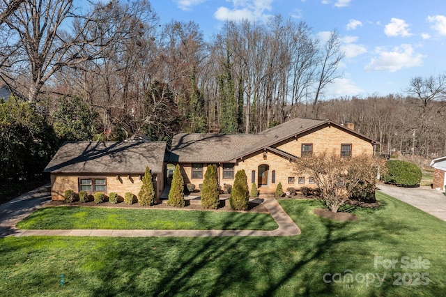 view of front of property featuring driveway, brick siding, a chimney, and a front yard