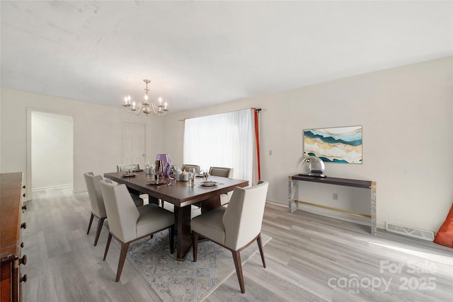 dining room with baseboards, light wood-style flooring, visible vents, and a notable chandelier