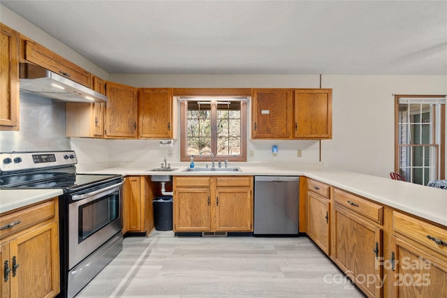 kitchen featuring under cabinet range hood, a sink, light countertops, appliances with stainless steel finishes, and brown cabinets