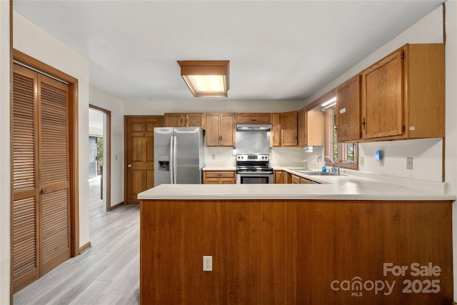 kitchen with under cabinet range hood, a sink, light countertops, appliances with stainless steel finishes, and brown cabinets