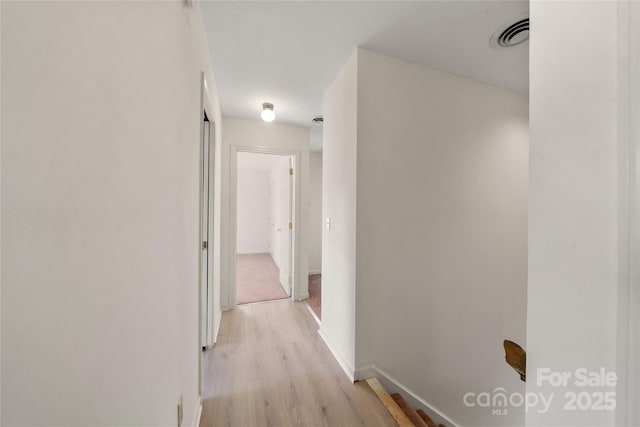 hallway featuring light wood-style floors, visible vents, and baseboards