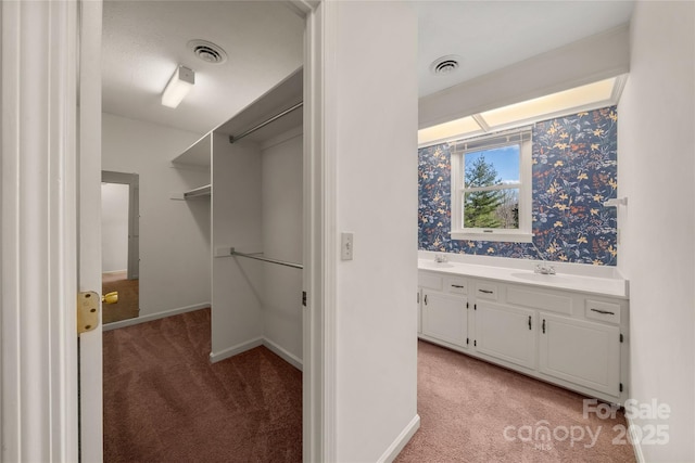 spacious closet featuring light colored carpet, visible vents, and a sink