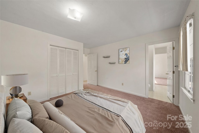 bedroom with baseboards, a closet, and light colored carpet