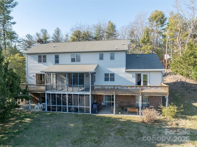 rear view of property featuring a sunroom, a wooden deck, a lawn, and a patio