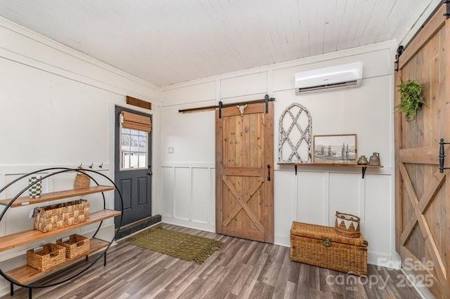 entryway with a barn door, a wall unit AC, a decorative wall, wood finished floors, and crown molding