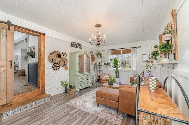 sitting room with a barn door, crown molding, an inviting chandelier, and wood finished floors