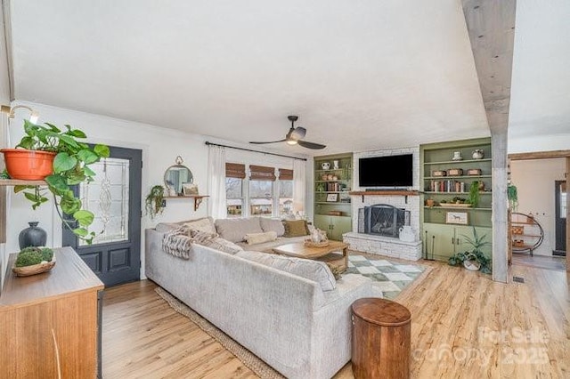 living room with light wood finished floors, ceiling fan, a fireplace, and built in features