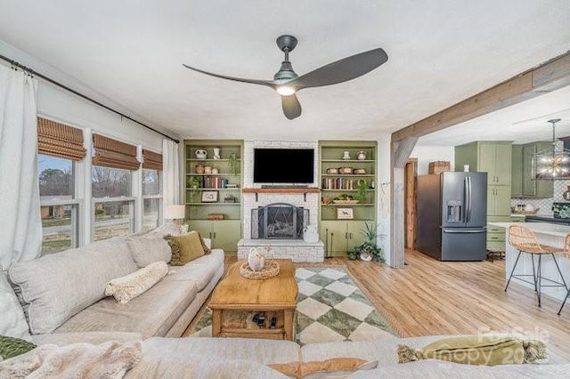 living area with ceiling fan with notable chandelier, a brick fireplace, and light wood-style floors