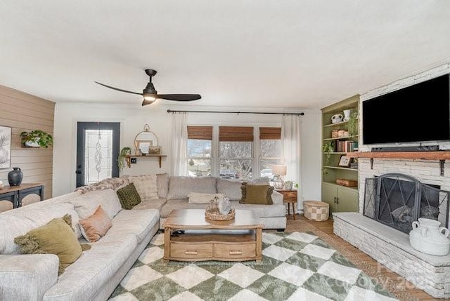 living area featuring built in features, ceiling fan, a stone fireplace, and wooden walls