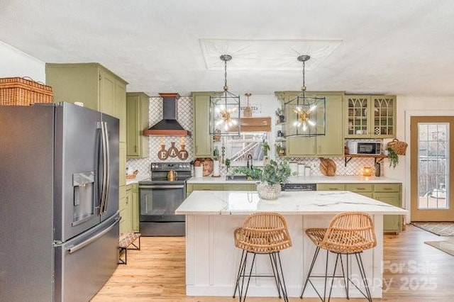 kitchen with wall chimney exhaust hood, light wood-style flooring, stainless steel refrigerator with ice dispenser, black range with electric cooktop, and green cabinets