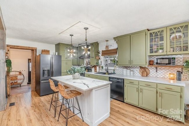 kitchen featuring a sink, black appliances, a kitchen island, green cabinetry, and a kitchen bar