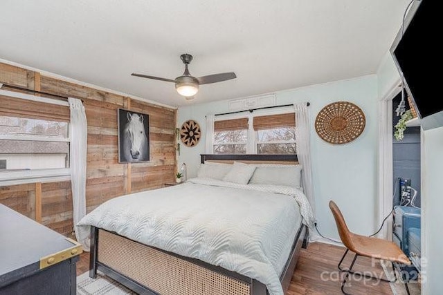 bedroom with ceiling fan, wood walls, and wood finished floors