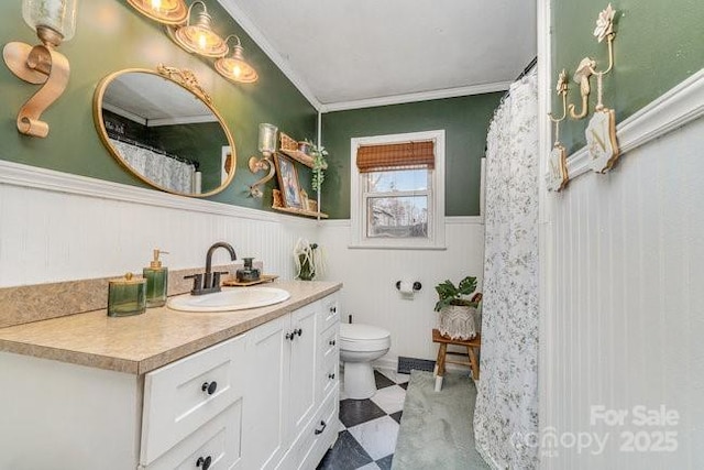 bathroom with toilet, a wainscoted wall, vanity, ornamental molding, and tile patterned floors