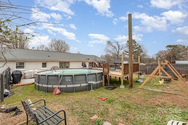 rear view of house featuring a deck, a playground, fence, a yard, and a fenced in pool