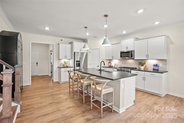 kitchen with premium appliances, dark countertops, an island with sink, hanging light fixtures, and a sink