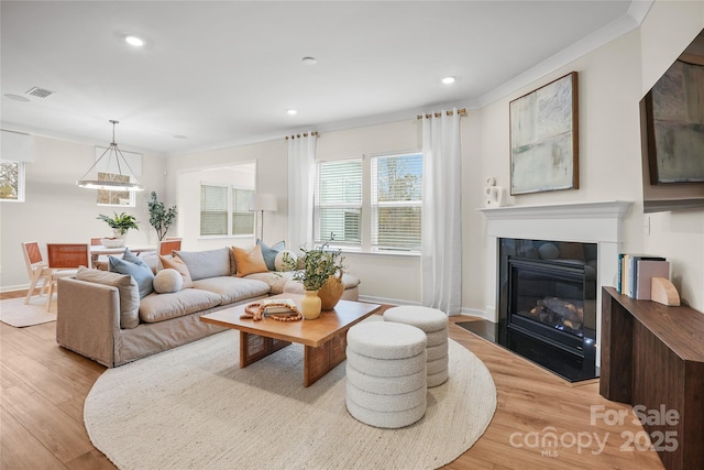 living area with visible vents, baseboards, light wood-type flooring, a glass covered fireplace, and crown molding