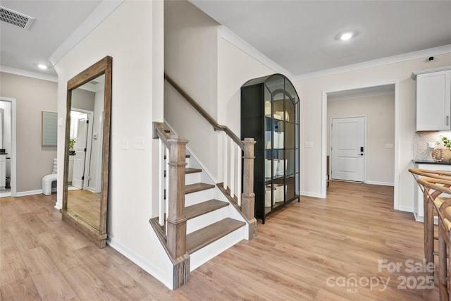 stairs with visible vents, crown molding, baseboards, and wood finished floors