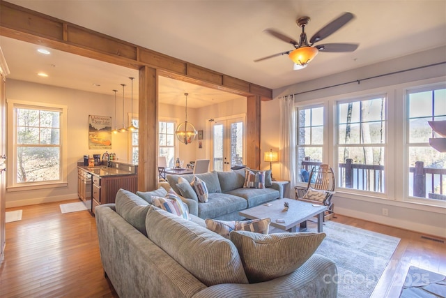 living room featuring light wood-style flooring, recessed lighting, ceiling fan with notable chandelier, visible vents, and baseboards