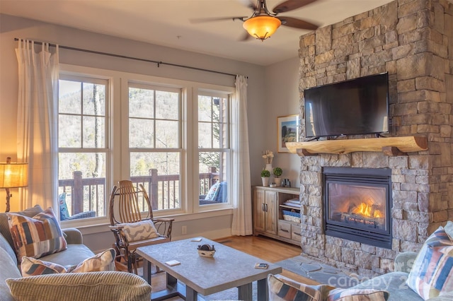 living area featuring a ceiling fan, wood finished floors, and a stone fireplace