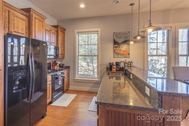 kitchen featuring light wood finished floors, brown cabinets, a peninsula, black appliances, and a sink