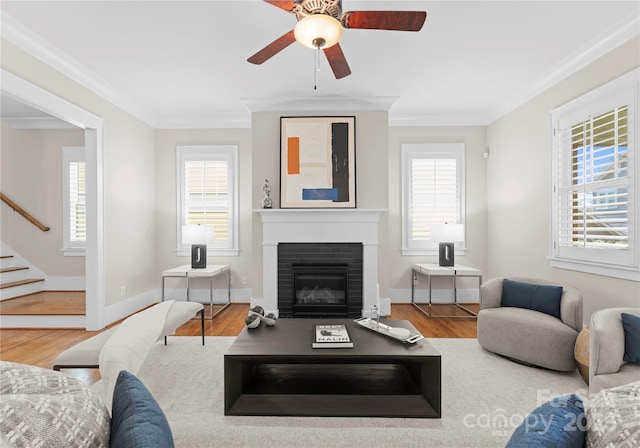 living room with wood finished floors, baseboards, stairs, crown molding, and a brick fireplace