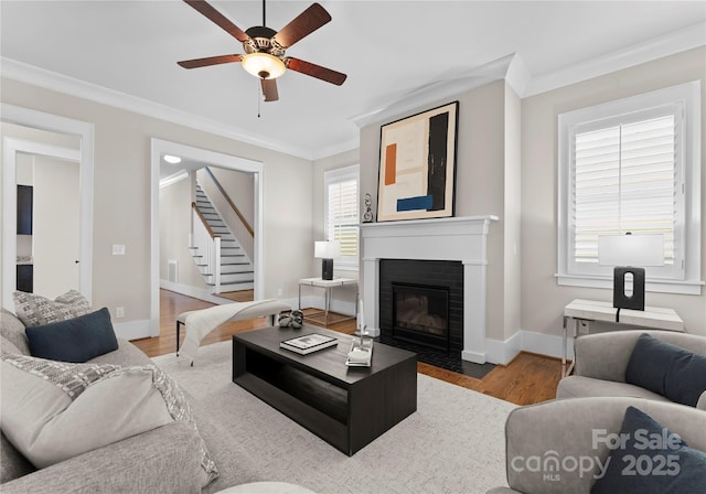 living room with ornamental molding, wood finished floors, a fireplace, baseboards, and stairs