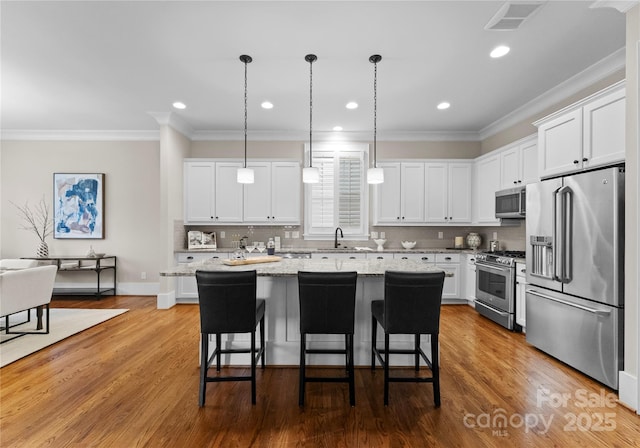 kitchen featuring stainless steel appliances, visible vents, a breakfast bar area, and white cabinetry