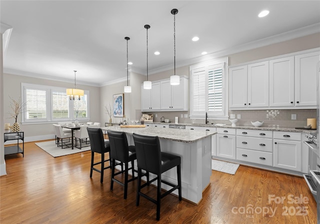 kitchen featuring light wood finished floors, ornamental molding, a kitchen island, and a sink