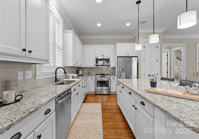 kitchen with wood finished floors, ornamental molding, a sink, white cabinets, and appliances with stainless steel finishes