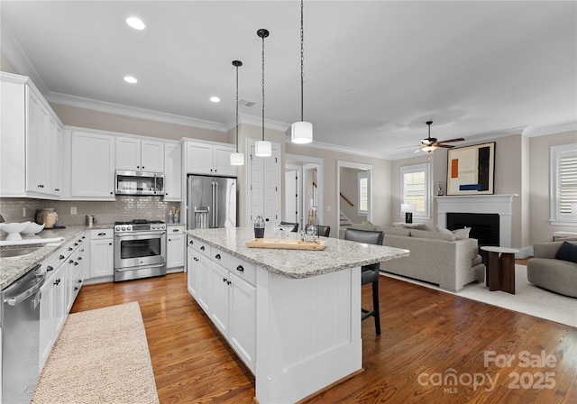 kitchen with dark wood-type flooring, a center island, stainless steel appliances, a fireplace, and crown molding