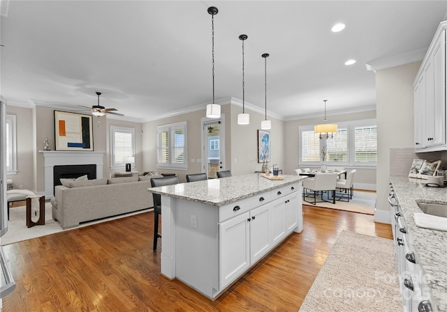 kitchen featuring a kitchen island, a fireplace, light wood-style floors, hanging light fixtures, and white cabinetry