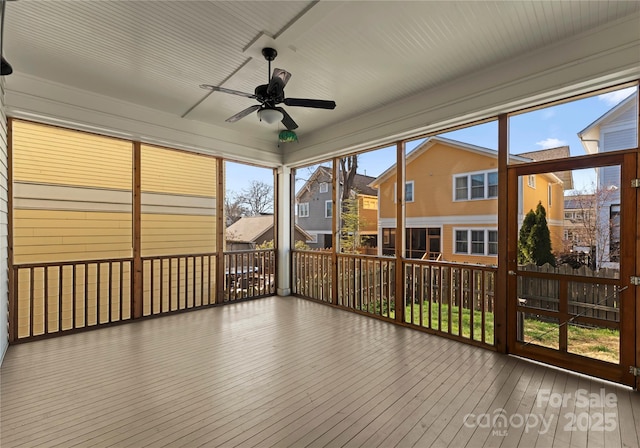 unfurnished sunroom featuring a residential view and a ceiling fan