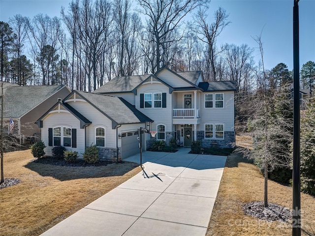 view of front of house with driveway, stone siding, a balcony, and a front lawn