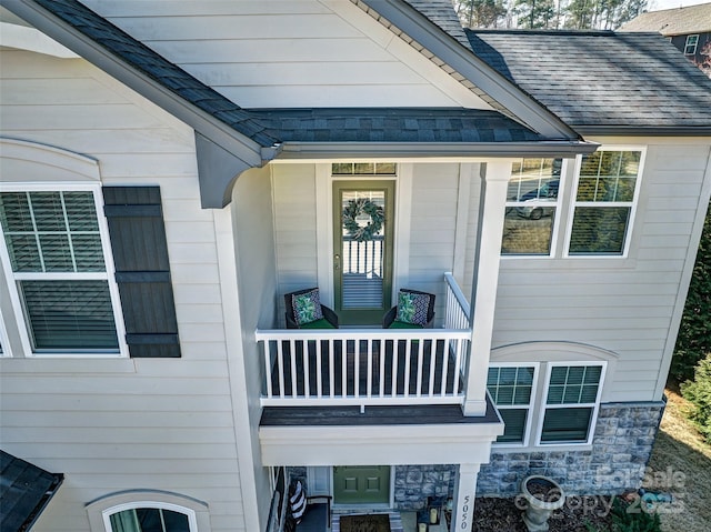 view of exterior entry featuring a shingled roof, stone siding, and a balcony