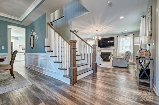 stairs with a decorative wall, a wainscoted wall, a fireplace, wood finished floors, and ornamental molding