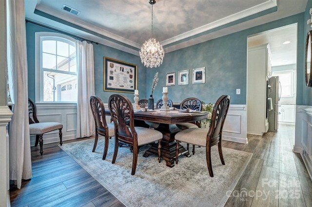 dining room featuring wood finished floors, a raised ceiling, and visible vents