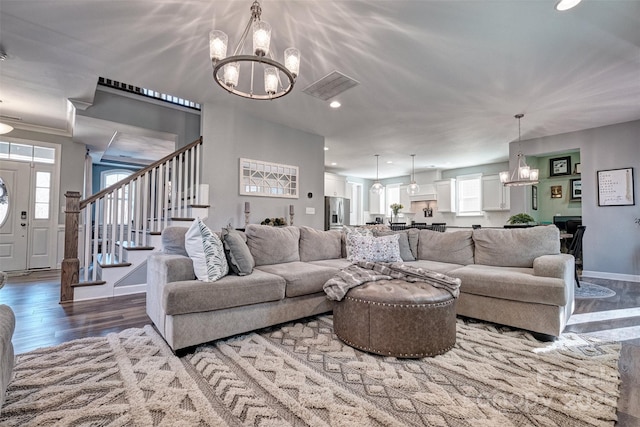 living room with wood finished floors, visible vents, a notable chandelier, and stairs