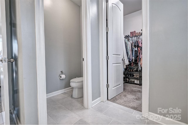 bathroom with a walk in closet, baseboards, and toilet